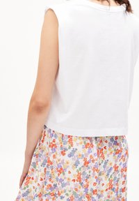 Kvinna klädd i en ärmlös vit topp och en plisserad kjol med ett flerfärgat blommönster, sedd från ryggen.