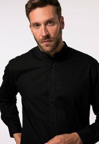 Camicia nera con colletto alla mandarino, realizzata in un tessuto liscio, con maniche lunghe e dettagli di cucitura discreti.