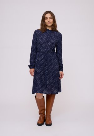 Navy floral dress with long sleeves, a collar, and a belted waist. Paired with brown knee-high boots and a textured fabric.