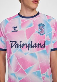 T-Shirt mit kurzen Ärmeln in einem bunten Muster aus pinkem, blauem und weißem zerbrochenem Glas. Enthält "Dairyland" in Dunkelblau und das Markenlogo.