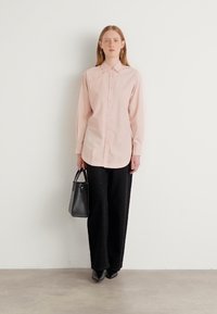 Light pink long-sleeve shirt with button front, paired with black wide-leg pants. The model holds a small black handbag. Smooth fabric texture.
