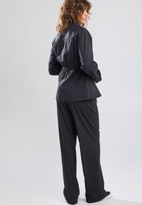 Black button-up shirt with a relaxed fit and gathered waist. Paired with loose black trousers and white sneakers. Soft fabric, simple design.