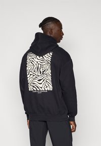 Sudadera negra con un gran patrón de cebra crema en la parte posterior, con el texto "HOGAR DEL FREERIDE" y "DESDE 2008" en blanco debajo del diseño.