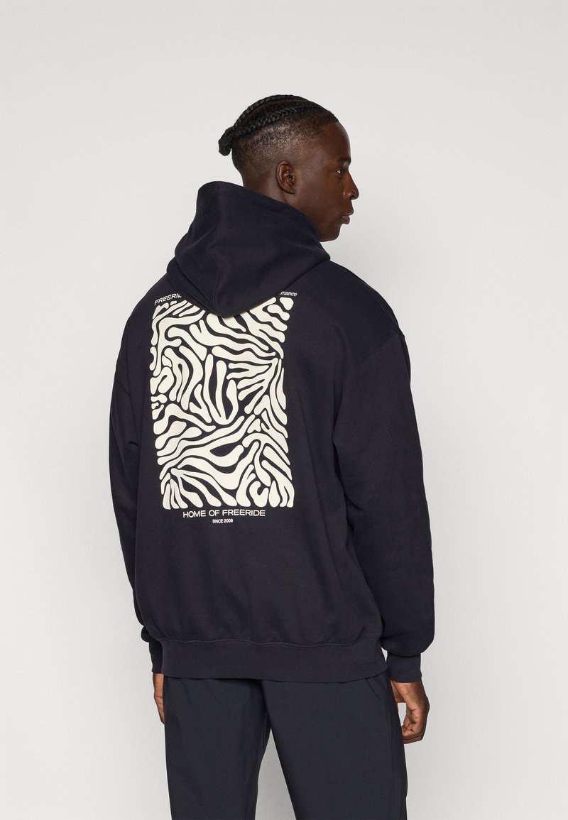 Sudadera negra con un gran patrón de cebra crema en la parte posterior, con el texto "HOGAR DEL FREERIDE" y "DESDE 2008" en blanco debajo del diseño.