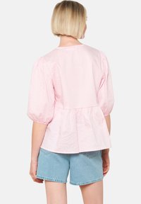 Blusa a quadri rosa con maniche a sbuffo, vita a peplo e scollatura rotonda; abbinata a pantaloni corti di denim. Tessuto di cotone morbido.