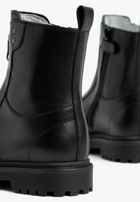 Black leather ankle boots with a smooth finish, featuring a zipper closure and textured rubber outsole for grip. Rear pull tab visible.