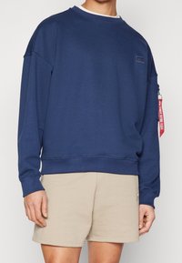 Felpa blu navy in cotone con scollo rotondo, maniche lunghe, polsini a costine e un piccolo logo a patch sul davanti.