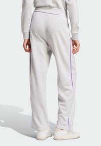 Szare dresowe spodnie o luźnym kroju, z fioletowymi paskami po bokach i ściągaczem w pasie. W połączeniu z jasnymi sportowymi butami.