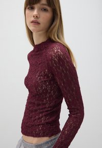 Bordeaux doorschijnend kant shirt met lange mouwen en hoge hals, met een textuur van bloemmotieven en een aansluitende pasvorm.