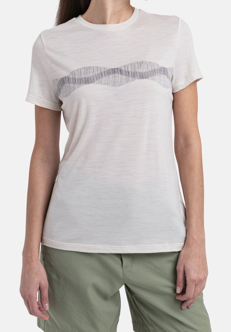 Ljusbeige t-shirt med kort ärm, mjuk textur, med ett vingligt mönster i mörkgrått över bröstet. Kombineras med gröna byxor.