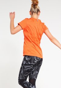 Camiseta deportiva naranja de manga corta combinada con leggings negros que presentan un patrón blanco en espiral. Tela suave, diseño ajustado, alta movilidad.
