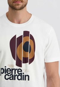 Weißes Baumwoll-T-Shirt mit einem mutigen grafischen Design aus Kreisen in Braun und Dunkellila, ergänzt durch schwarzen Text mit der Aufschrift "pierre cardin 1954."