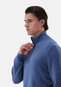 Helles blaues, gestricktes Sweatshirt mit hohem Kragen und halbem Reißverschluss. Verfügt über strukturierten Stoff und gerippte Bündchen für zusätzliche Details.