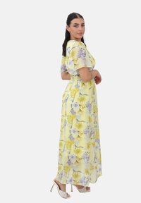 Blomster maxi kjole i gul med lilla og hvide blomster, korte flagrende ærmer, elastisk talje og ankel-længde silhuet.