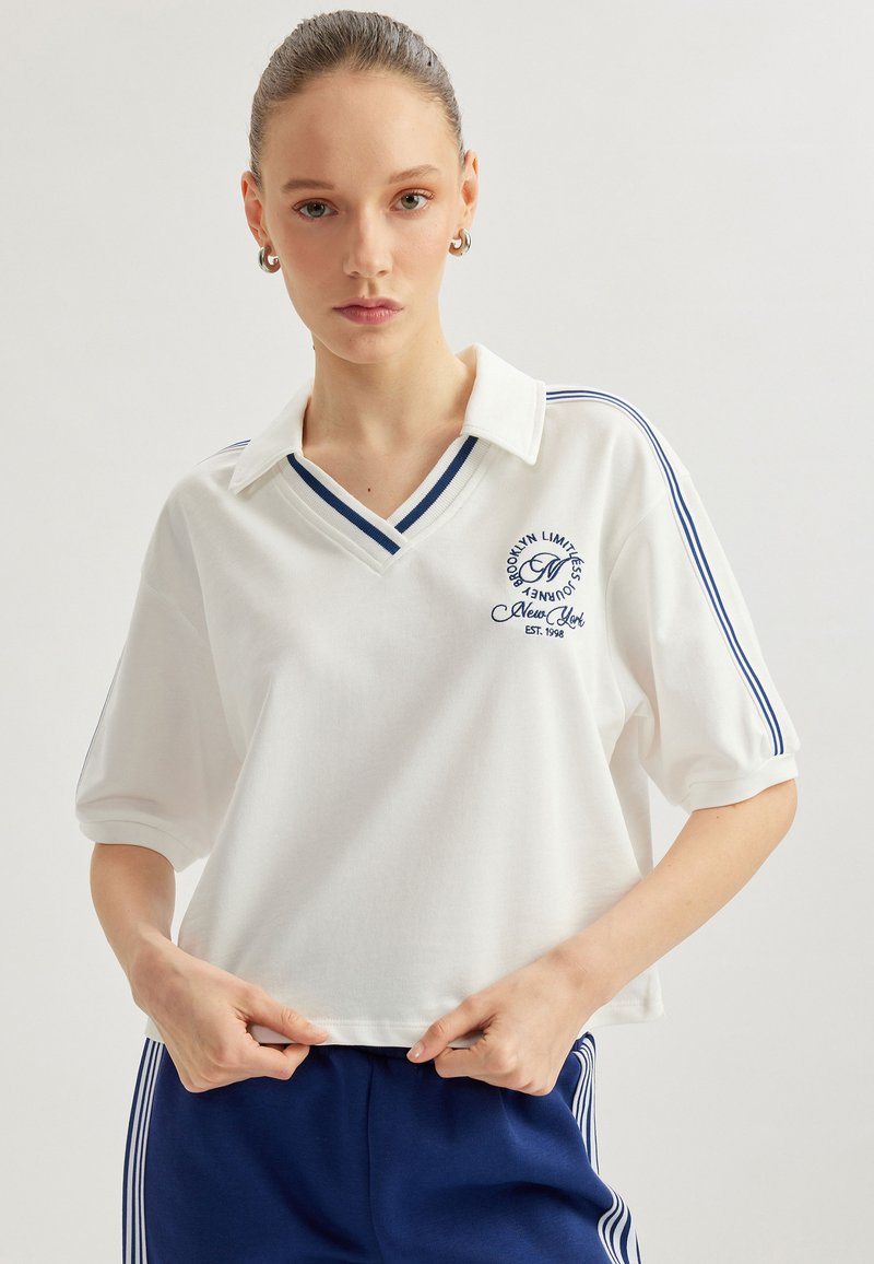 Witte katoenen polo met een V-hals, blauwe gestreepte accenten op de mouwen en een geborduurd logo. Korte mouwen en een ontspannen pasvorm.
