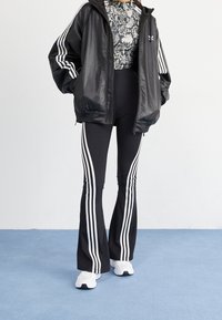 Svart läderjacka med huood, mönstrad svart och vit topp, svarta utsvängda leggings med tre vita ränder, samt vita sportskor.