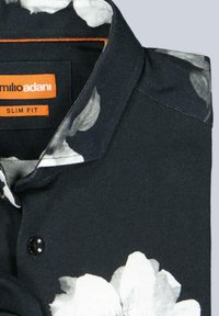 Schmal geschnittenes Hemd aus schwarzem Stoff mit einem weißen Blumenmuster am Kragen, einem schwarzen Knopf und einem orangefarbenen Markenetikett.