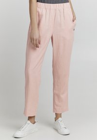 Lys rosa linbukser med elastisk midje, sidelommer og rett snitt, kombinert med hvite sneakers for et avslappet utseende.