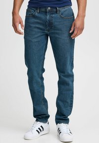 Jeans de mezclilla azul oscuro con un diseño de pierna recta, estilo de cinco bolsillos y detalles de costura en contraste. Combinados con zapatillas blancas.