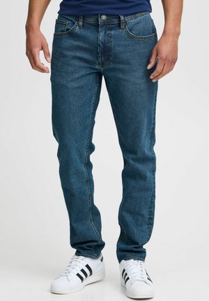 Mørkeblå denimjeans med rette ben, fem lommer og kontraststing. Kombinert med hvite sneakers.
