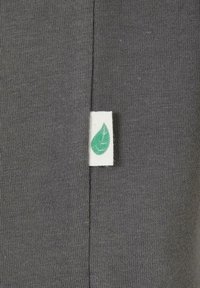 Grau strukturierter Stoff mit einem kleinen weißen Etikett, das ein grünes Blätterdesign zeigt, an der Seite angebracht.