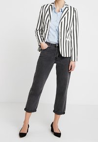 Pruhované černobílé sako, světle modrá košile na knoflíky, zrolované černé džíny a černé vysoké podpatky. Moderní střih s přizpůsobeným designem.