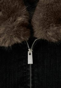 Černá denimová bunda s hnědým umělým kožešinovým límcem a stříbrným zipem. Zip má obdélníkovou táhlo. Viditelná texturovaná tkanina.