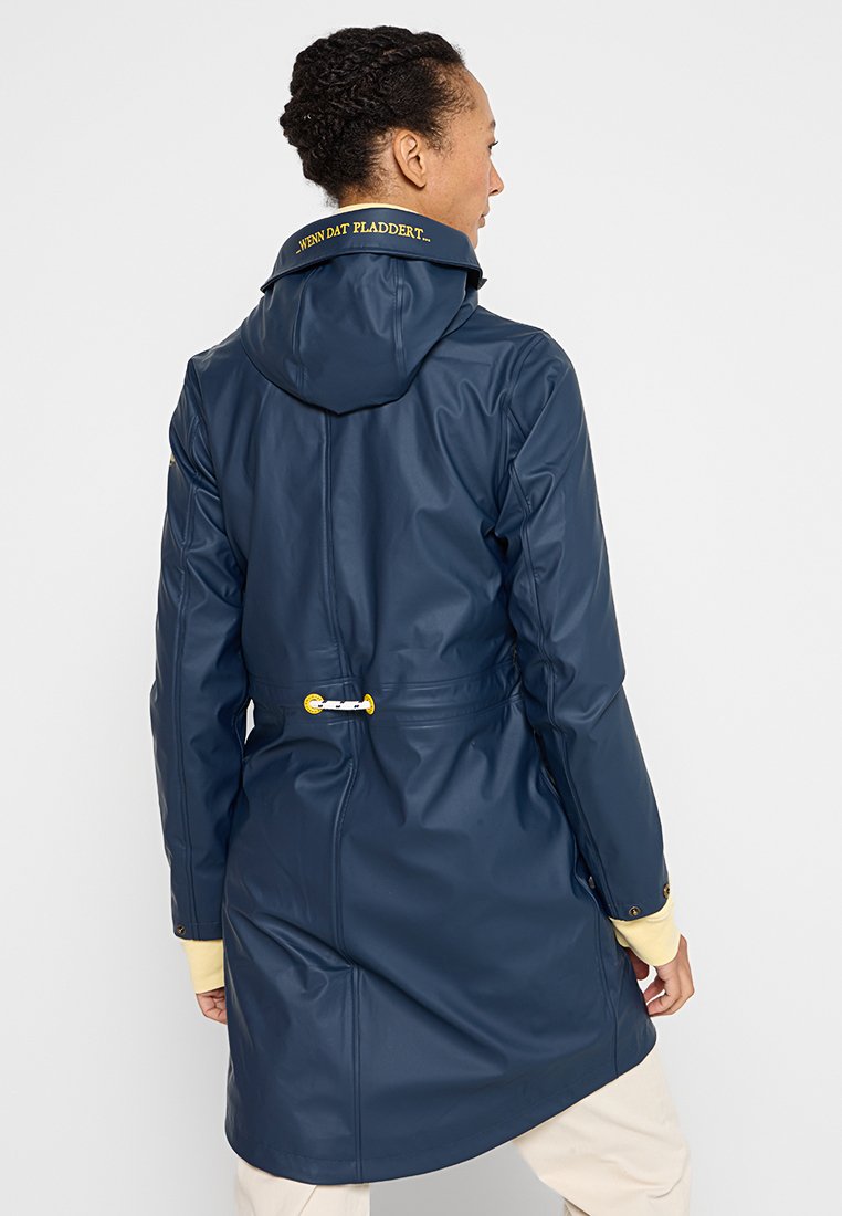 Impermeabile blu navy con cappuccio, cordoncino in vita regolabile, dettagli gialli e logo sul colletto. Texture liscia e lucida.