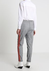 Šedé kostkované kalhoty s elastickým páskem, které mají kontrastní červené boční pruhy, zúžený střih nohou a hladkou texturu.