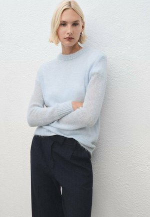Maglione lavorato a maglia blu chiaro con maniche testurizzate, indossato sopra pantaloni scuri a righe. Il materiale sembra morbido e leggermente trasparente.