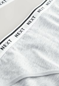 Grå bomuldsunderbukser med en blød tekstur. Har et sort-accentueret elastikbånd med teksten "NEXT" i gentaget mønster. Glatte kanter og enkelt design.