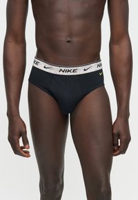 Αρσενικός κορμός με μαύρα εσώρουχα Nike, με λευκή ζώνη μέσης με πολύχρωμες κηλίδες και μαύρα λογότυπα Nike.