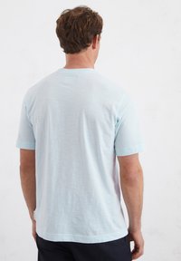 Lichtblauw t-shirt met korte mouwen, met een gestructureerde afwerking en ronde hals. Inclusief een klein label near de zoom en een subtiele kleurovergang.