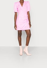 Růžové zavinovací šaty s nabranými rukávy a květinovými vzory, doplněné o světle růžové kotníkové boty. Hladká textura a přiléhavý design.