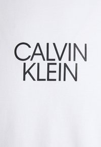 Camiseta de algodón blanca con el texto negro en negrita "CALVIN KLEIN" en una fuente moderna. Textura suave con un corte clásico.