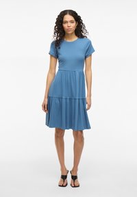 Robe bleue à manches courtes avec un corsage ajusté et une jupe à volants. Fabriquée en tissu doux, elle possède une texture lisse et un design décontracté.