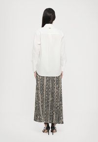 Hvit langermet skjorte med bakfold, kombinert med et gulvlengde skjørt i slangeskinnsmønster. Stoffet ser lett og luftig ut.