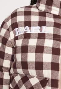 Brązowa i kremowa pikowana kurtka w kratę z wysokim kołnierzem i haftem 'WARL' na lewej piersi. Miękka tekstura i luźny krój.