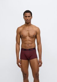 Cuecas boxer vermelhas com padrão e cós preto com a marca "HUGO". Apresentam um corte justo e tecido com textura suave.