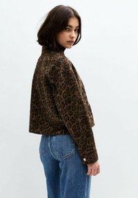 Leopardenmuster-Crop-Jacke in Braun und Schwarz, aus weichem Material gefertigt; verfügt über einen hohen Kragen und Knopf-Akzente an den Ärmeln.