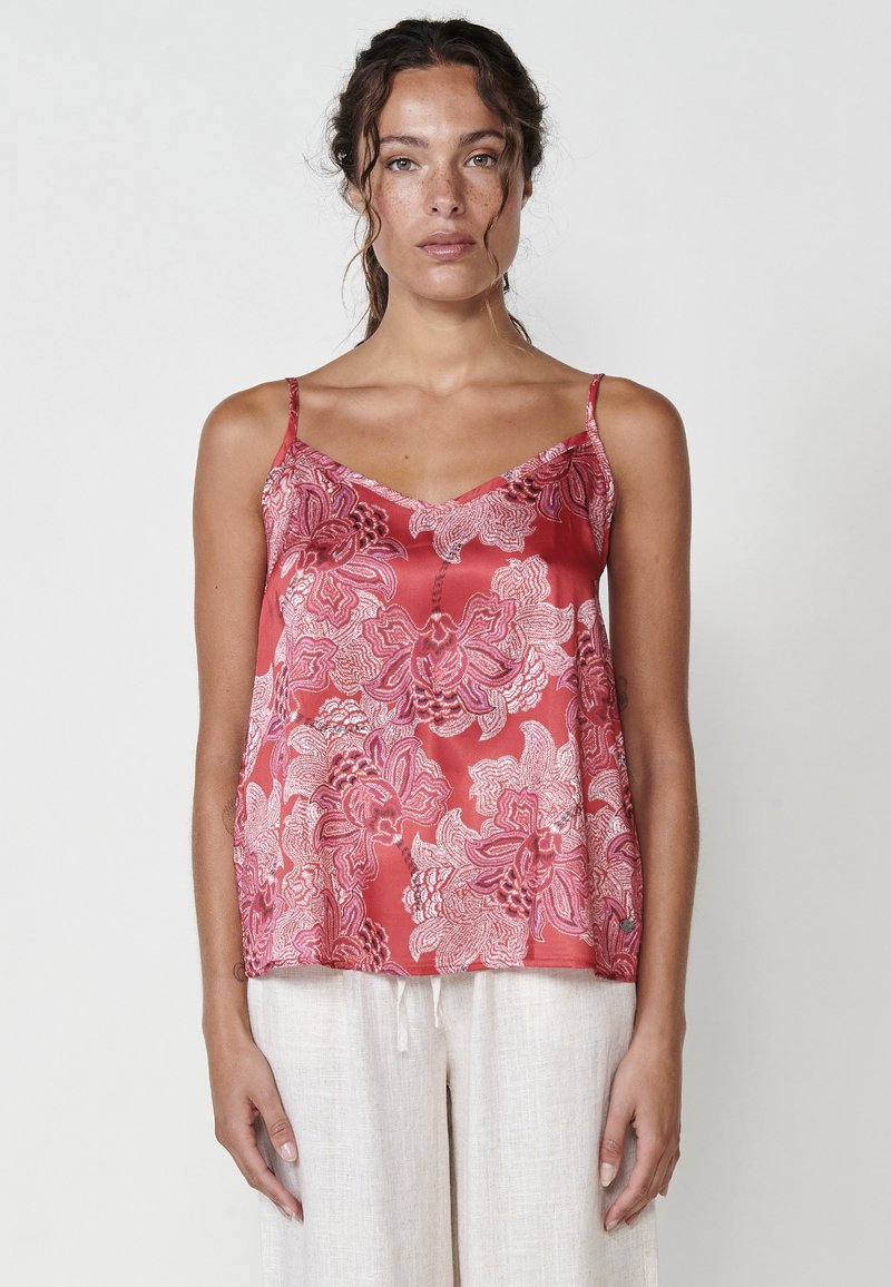 Camisole en satin avec broderie florale dans des tons de rose et de blanc, dotée de fines bretelles et d'un design en V, associée à un pantalon en lin léger.