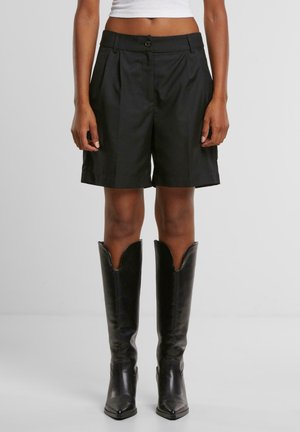 Black tailored shorts made of a smooth fabric with pleats, paired with knee-high black leather boots featuring a square toe and pointed top.