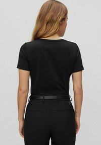 Musta lyhythihainen T-paita, jossa on pyöreä kaulus, valmistettu sileästä puuvillasta, yhdistettynä istuviin mustiin housuihin, jotka on kiinnitetty ohuella vyöllä.