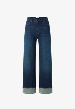 Sötétkék, világosra mosott árnyalattal rendelkező bőszárú farmernadrág. Magasított derékrésszel, világosabb kék színű felhajtott szegéllyel és klasszikus varrással rendelkezik.