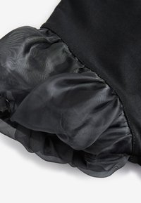 Vestido negro con un dobladillo de malla negra con volantes. La tela principal es suave, mientras que el volante añade textura y volumen en el borde inferior.