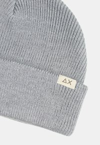 Berretto lavorato a maglia grigio con risvolto, caratterizzato da una leggera trama in tessuto e un piccolo etichetta con un logo.
