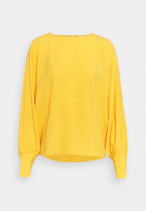 Żółta bluzka z długim rękawem, okrągłym dekoltem, marszczonymi bufkowatymi rękawami i dopasowanymi mankietami, prezentowana na jednolitym jasnym tle.