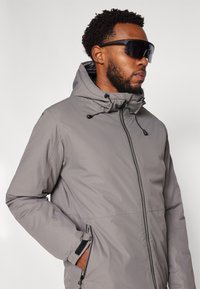 Graue Kapuzenjacke mit durchgehendem Reißverschluss, verstellbarem Kordelzug und Seitentaschen. Glattes Gewebe mit einer dezenten Textur.