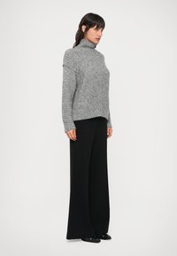 Jersey de cuello alto gris de punto con un corte holgado, combinado con pantalones anchos negros. La tela tiene una sutil textura y un diseño relajado.