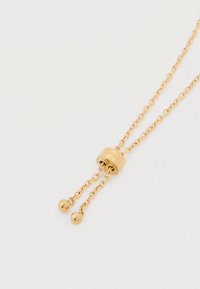 Auksinio tono kaklo papuošalas su metaliniu užsegimu, turintis dvi grandinėles ir apvalių karoliukų akcentus. Lygi tekstūra, minimalistinis dizainas, universalus siluetas.